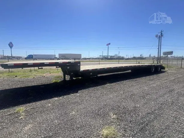 Long flatbed trailer parked on gravel under a clear blue sky