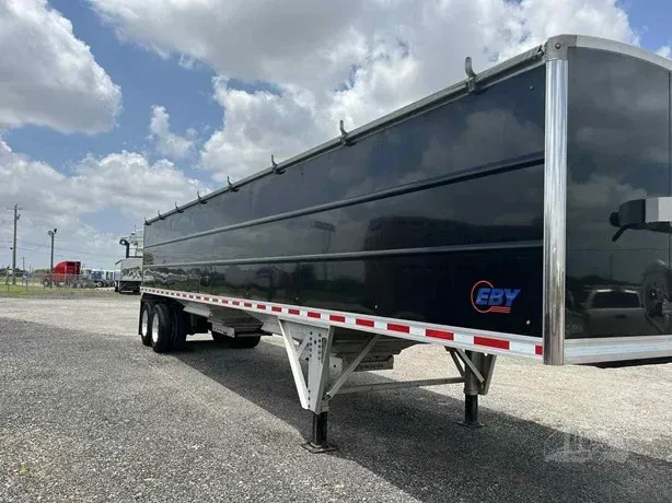 Black dump trailer parked on gravel lot under a cloudy sky
