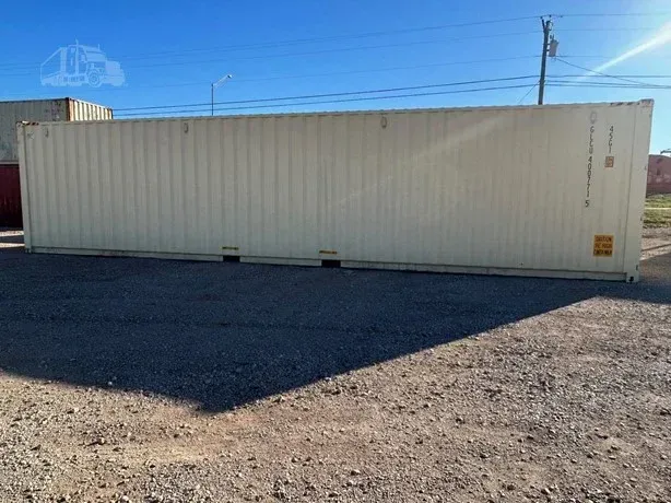 Long white shipping container on a gravel lot under a clear blue sky