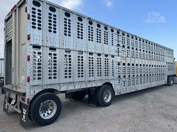Silver livestock trailer parked on pavement under a blue sky