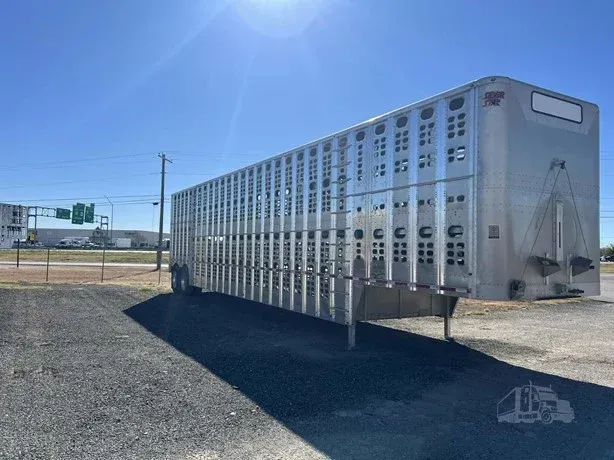 Silver livestock trailer in a sunny open lot with a road sign in the background