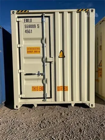 White shipping container with black ID markings and a warning sign on a gravel lot under blue sky.