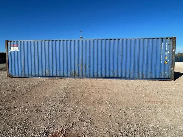 Blue shipping container on a gravel lot under a clear sky.