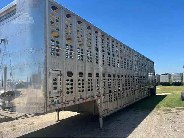 Silver livestock trailer parked on grass under a clear blue sky