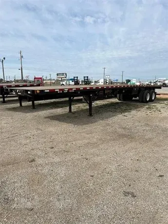 Flatbed trailer parked on a gravel lot under a cloudy sky