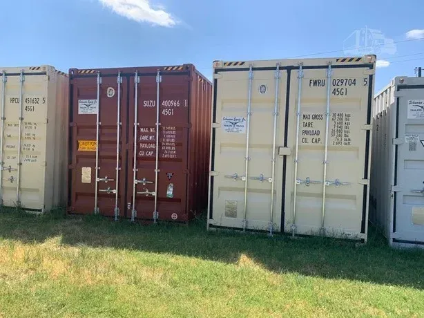 Row of shipping containers in a grassy yard, including red, beige, and white containers.