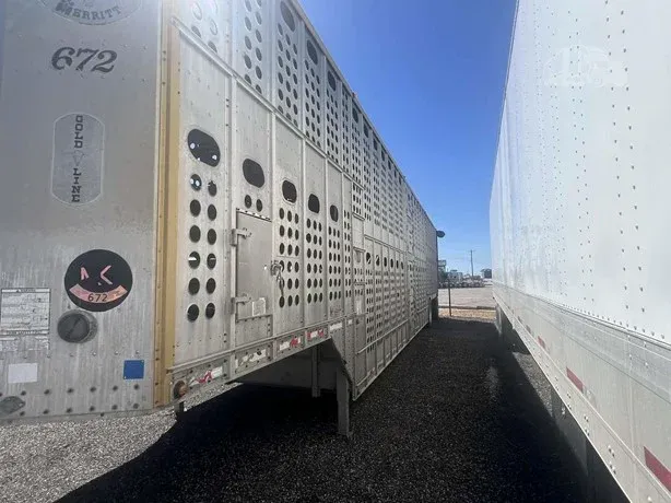 Two silver livestock trailers parked side by side on a gravel lot under a clear sky.