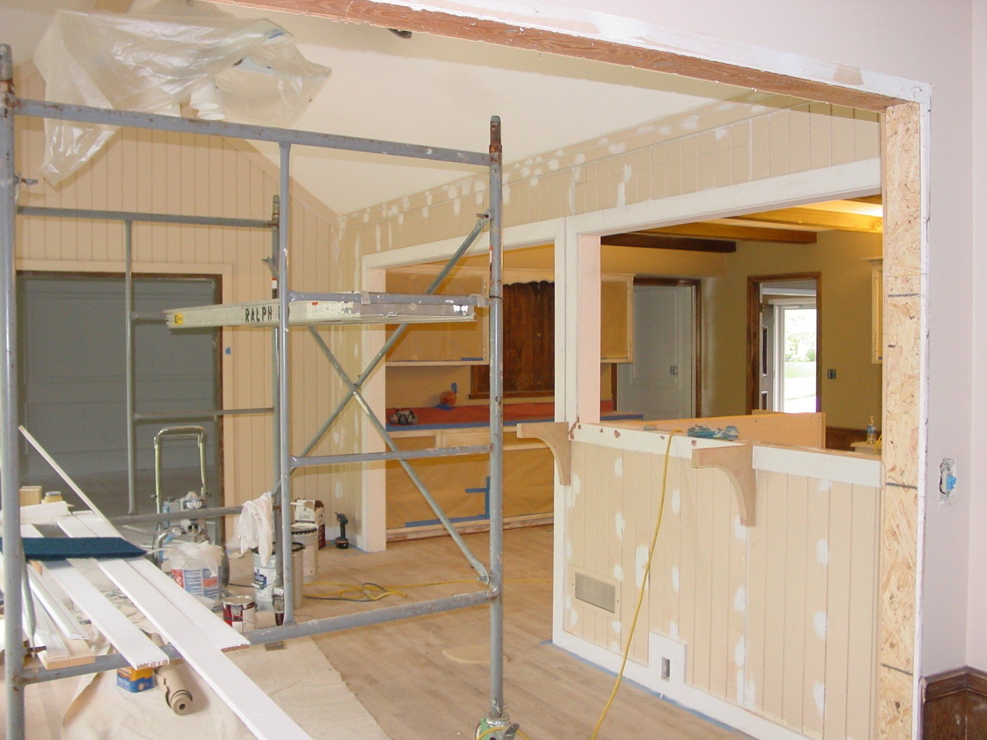 Interior room under renovation, with scaffolding, wood paneling, and open doorways.