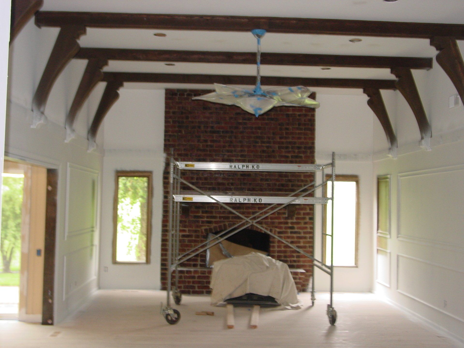 Room with brick fireplace, scaffolding, exposed beams, and decorative trim.