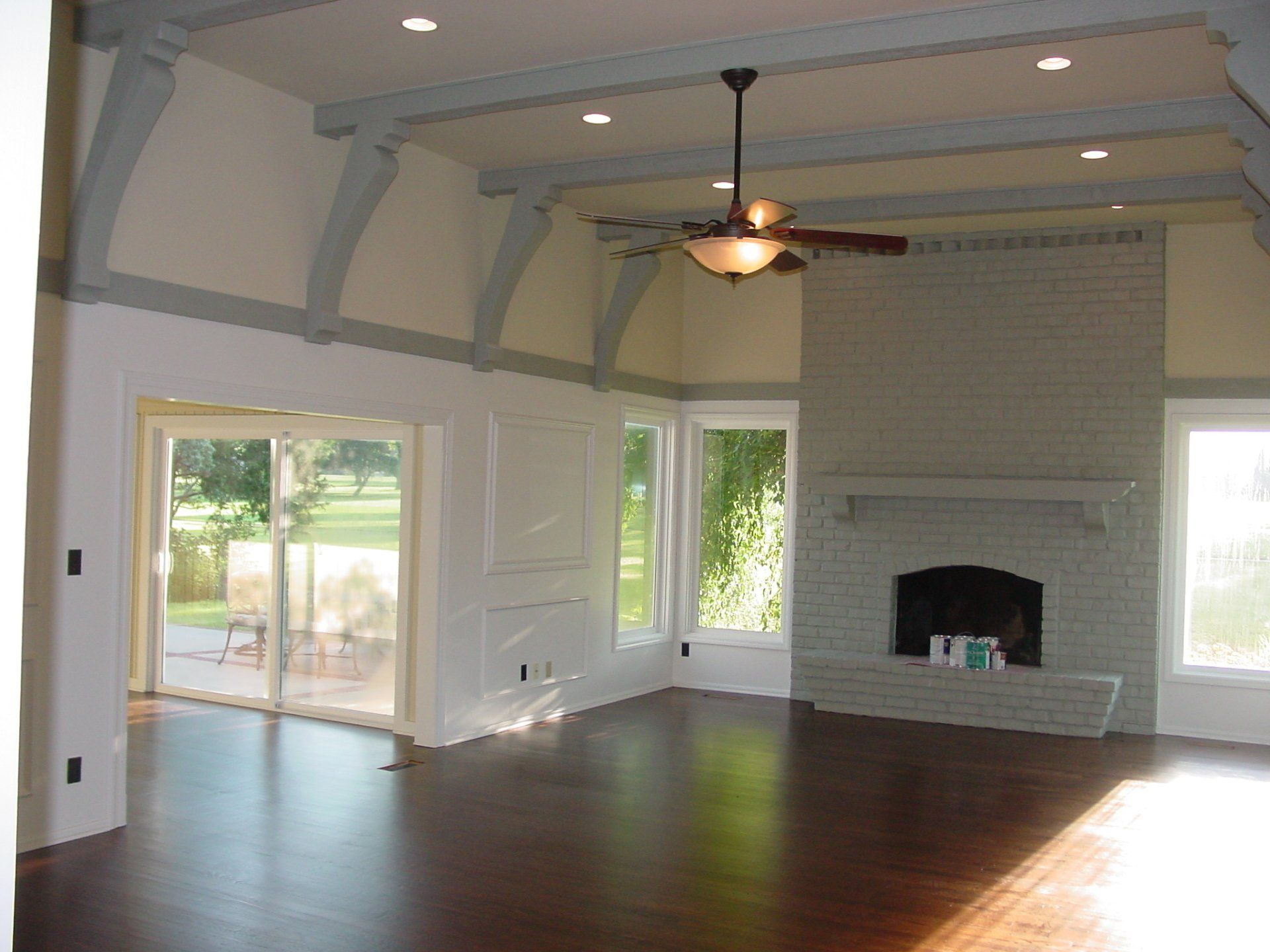 Empty living room with dark wood floor, white brick fireplace, and light blue ceiling beams.