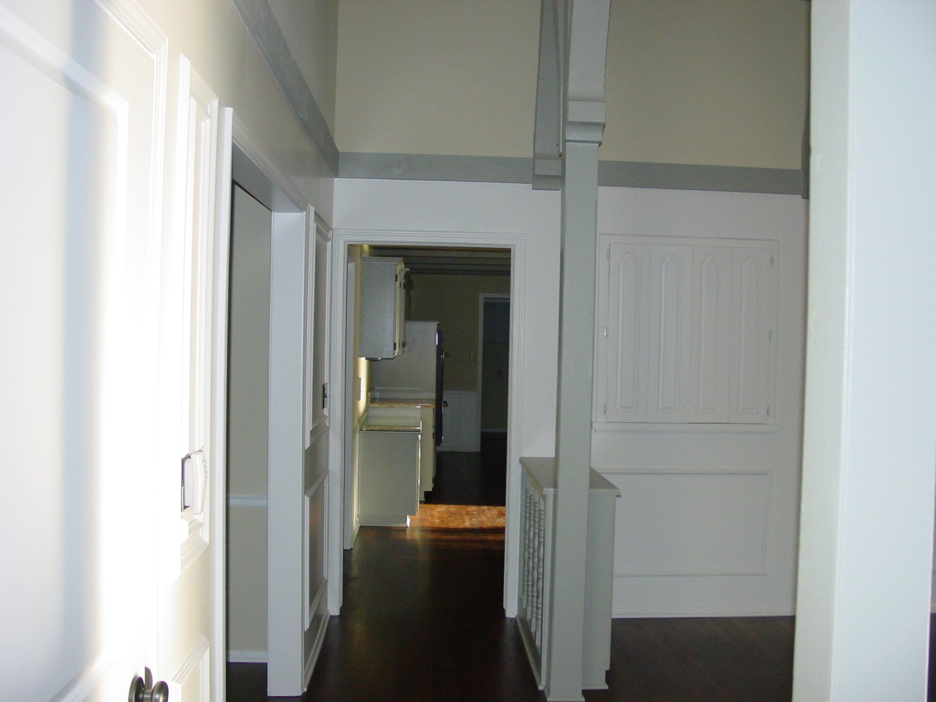 Hallway with dark wood floor, white walls and doors, light entering from the left.