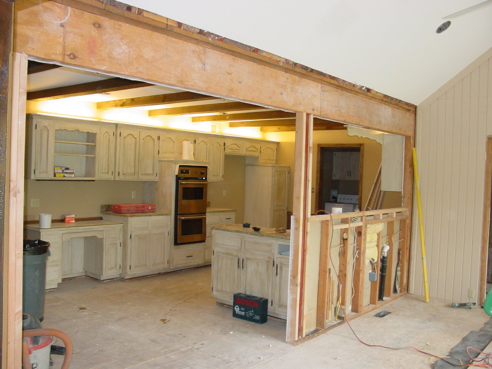 Kitchen remodel: Partially demolished wall reveals cabinetry and appliances. Studs exposed on right.