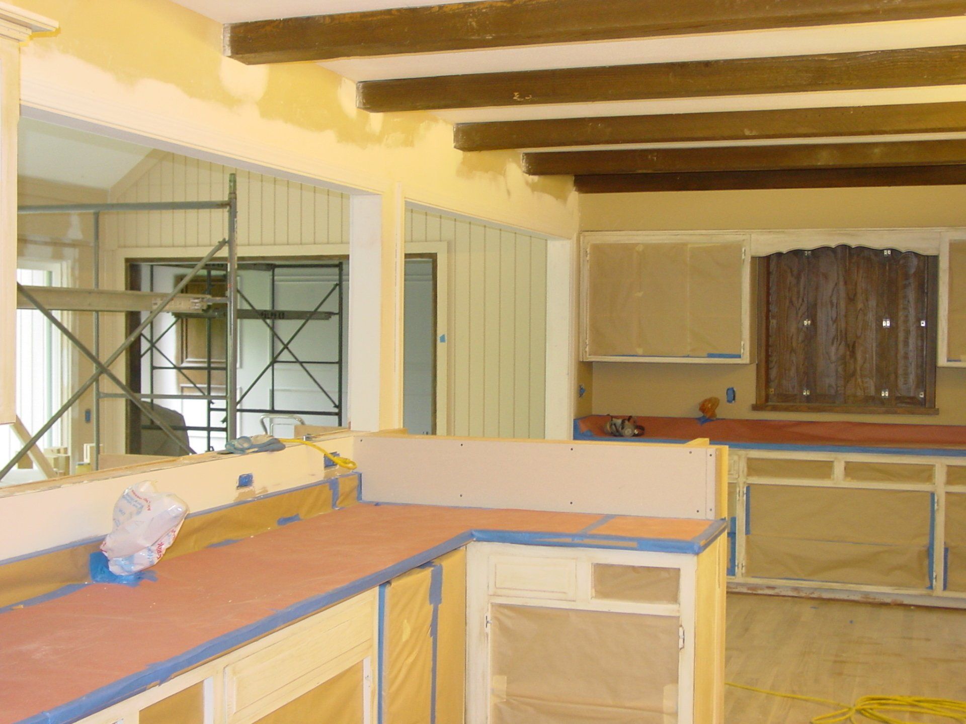 Kitchen under construction with exposed beams, cabinets, and a counter covered in protective material.
