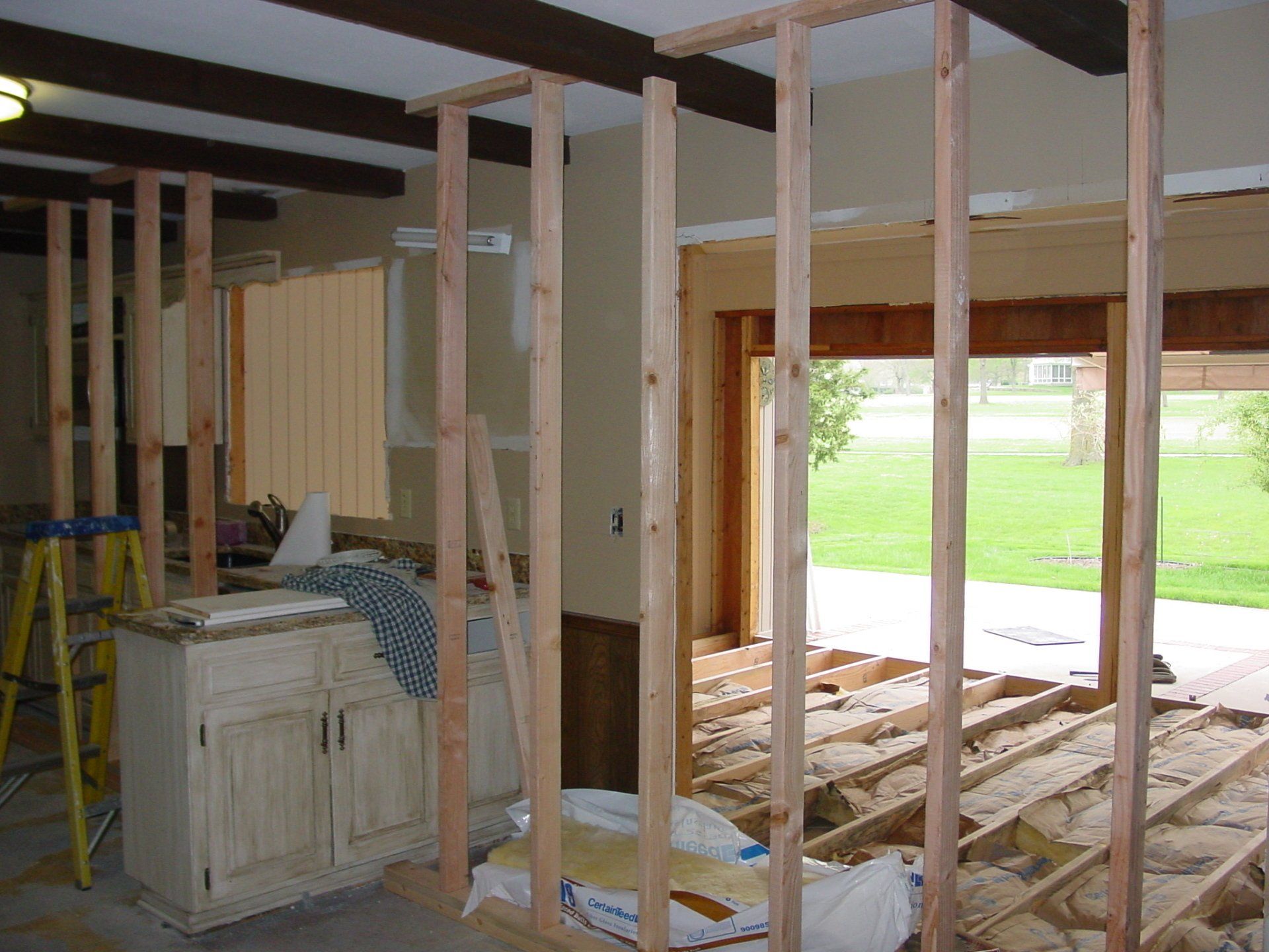 Interior renovation with exposed wall studs, flooring, and cabinets. A doorway and window lead to outside.