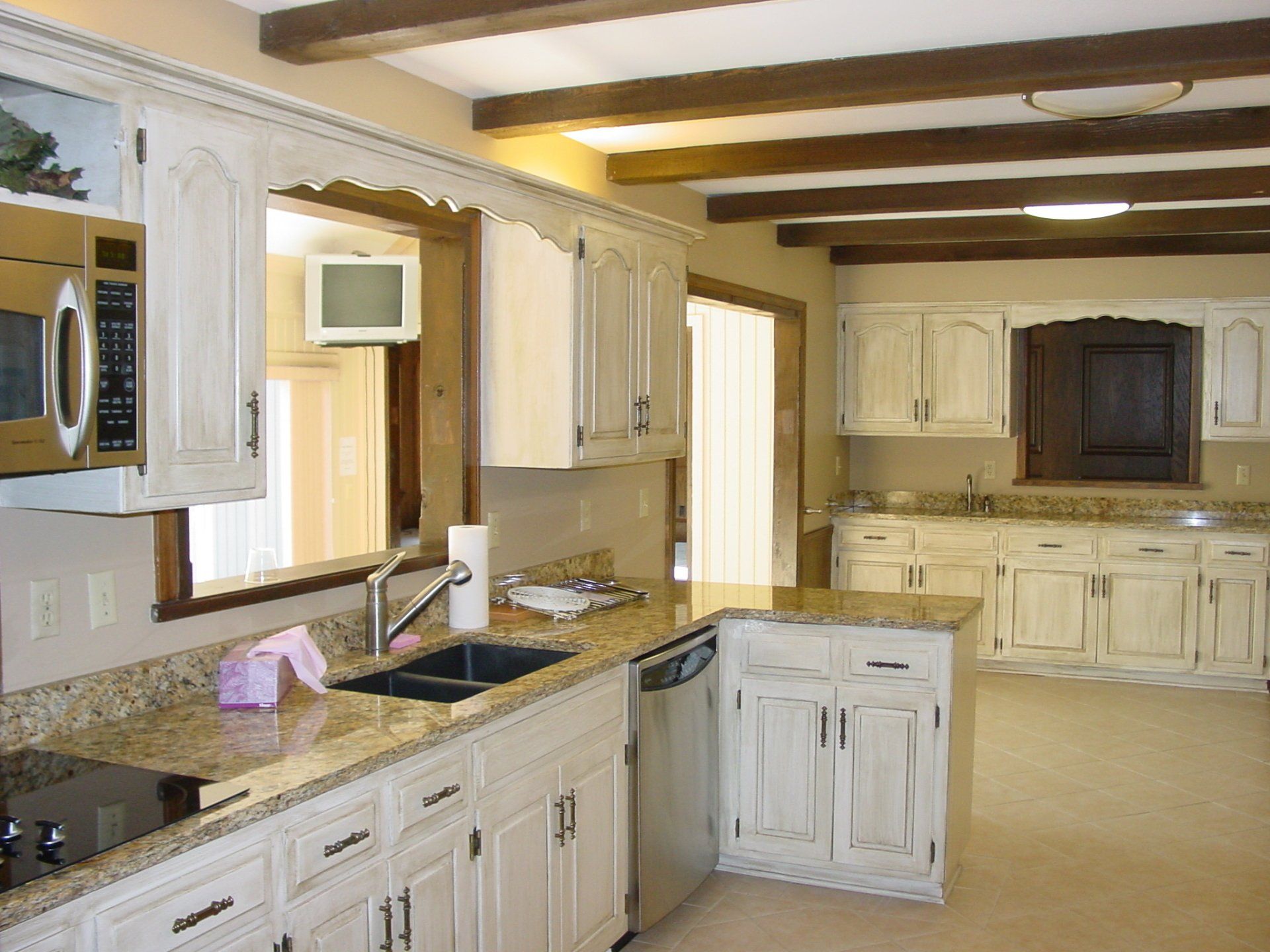 White kitchen with wood beam ceiling, granite countertops, and light-colored cabinets.