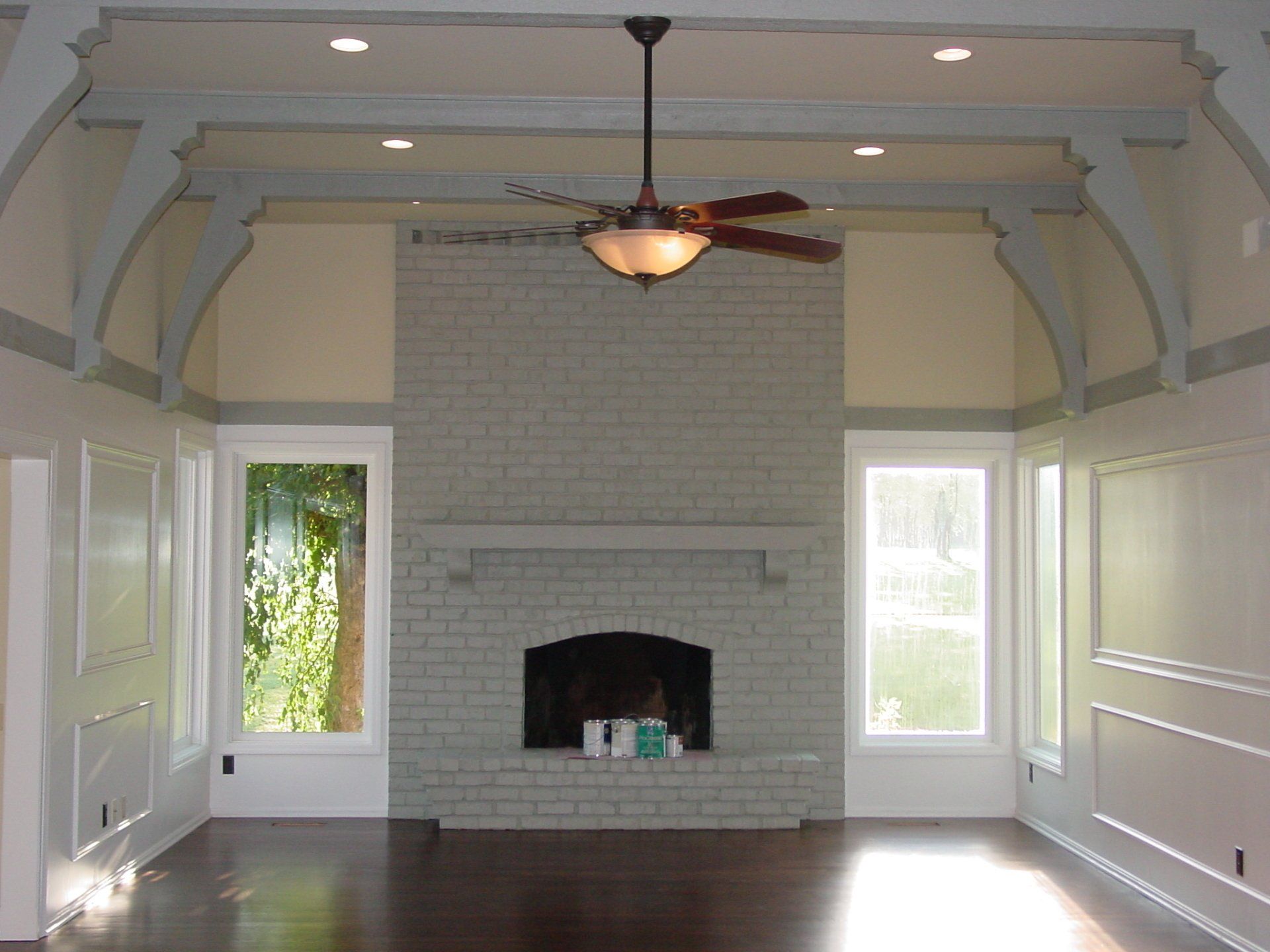 Living room with white brick fireplace, dark wood floor, windows, and ceiling fan.