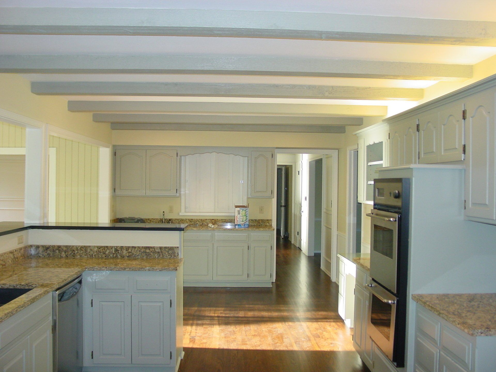 Kitchen with light blue cabinets, granite countertops, wood floors, and exposed ceiling beams.