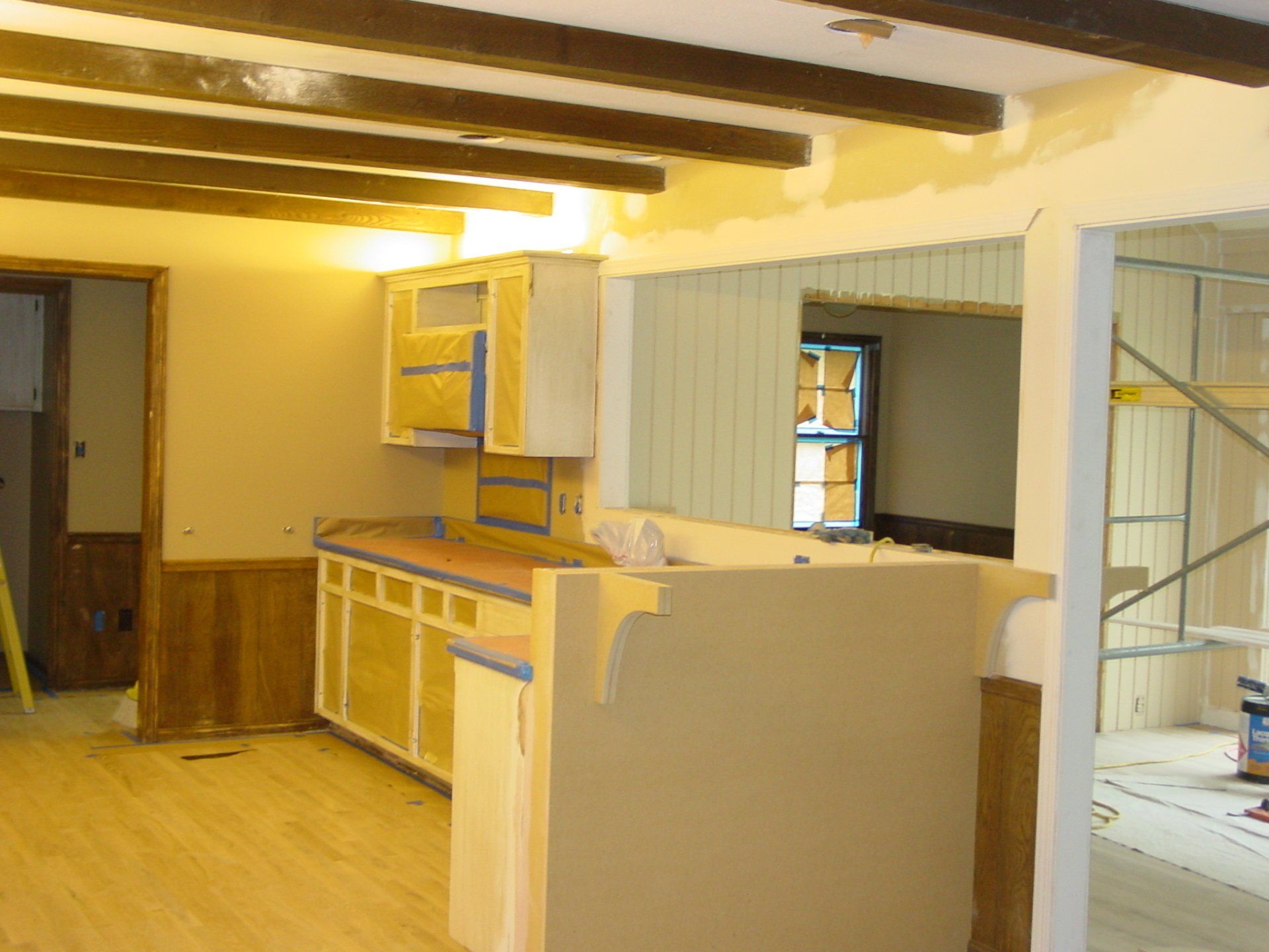 Kitchen under renovation, light wood floors, cabinets, and a pass-through opening.