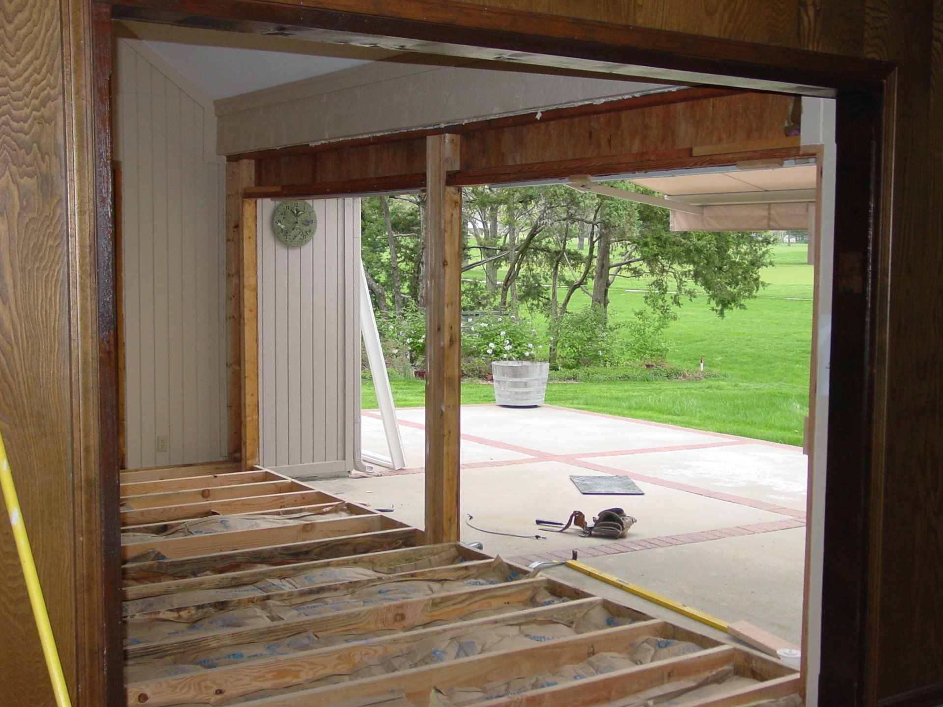 Interior view of a doorway being remodeled, revealing outside patio and yard. Wooden framing, exposed beams.