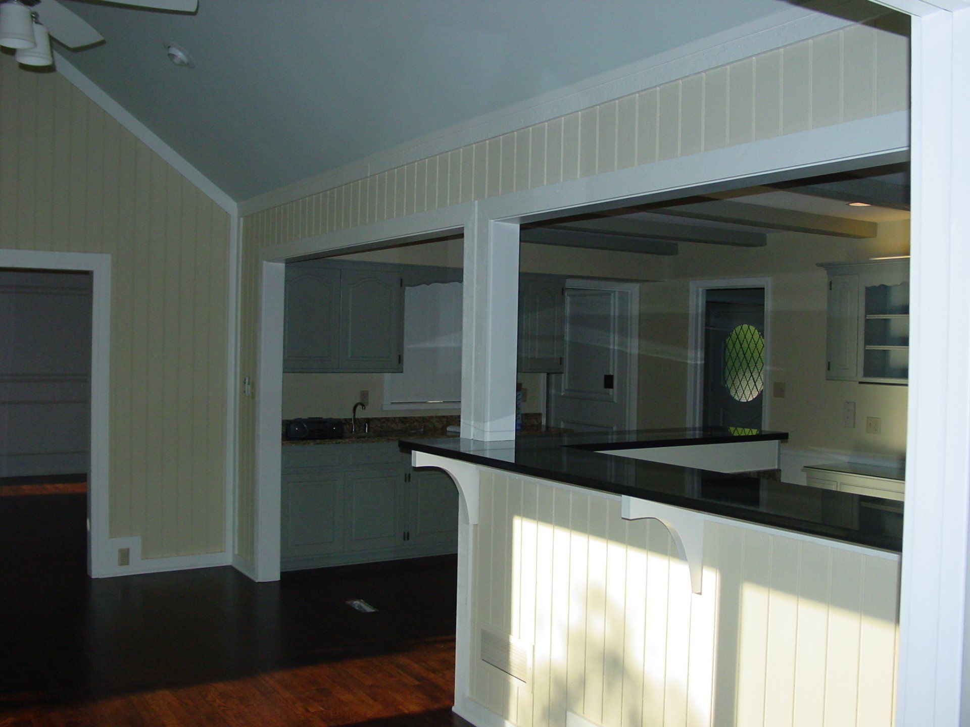 Interior view of a kitchen and living area, with a breakfast bar, light walls, and dark wood floors.