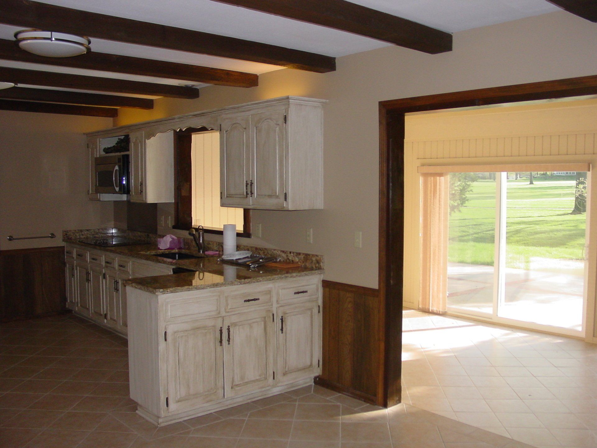 Kitchen with light-colored cabinets, granite countertops, and a view through sliding doors to a green lawn.