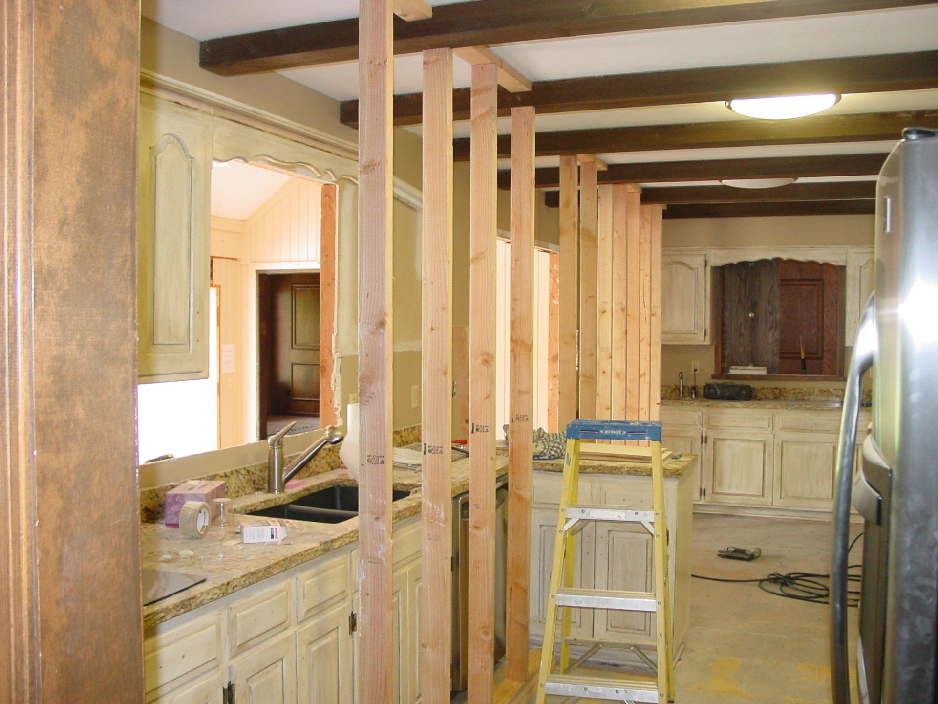 Kitchen under renovation, with exposed wooden studs for a partial wall, cabinets, and a ladder.