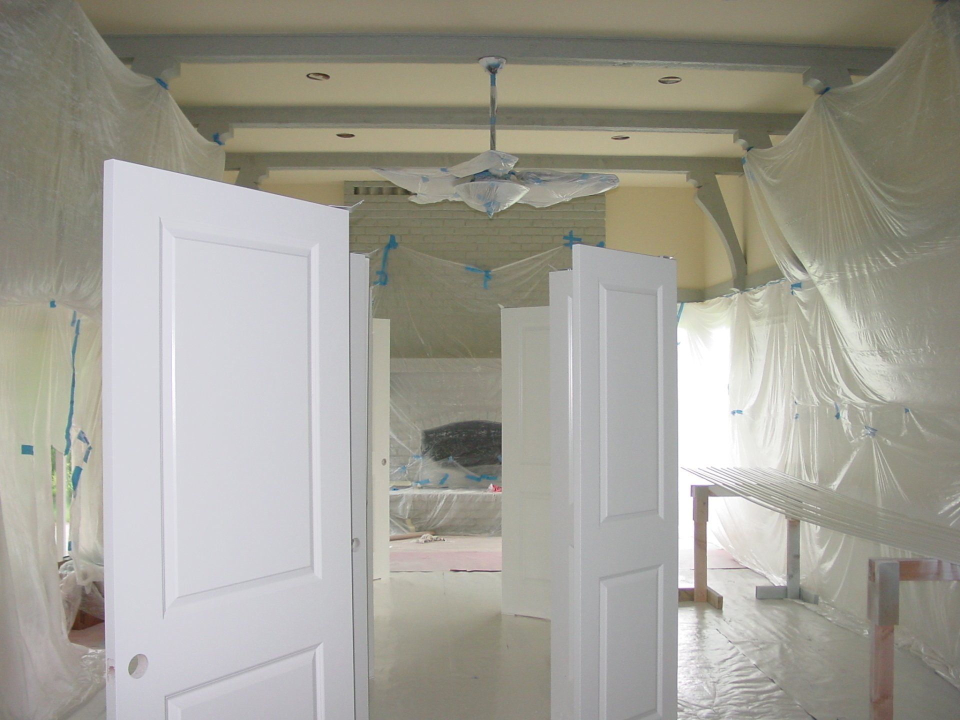 Interior room with white-painted doors, draped with plastic, possibly for painting or renovation.