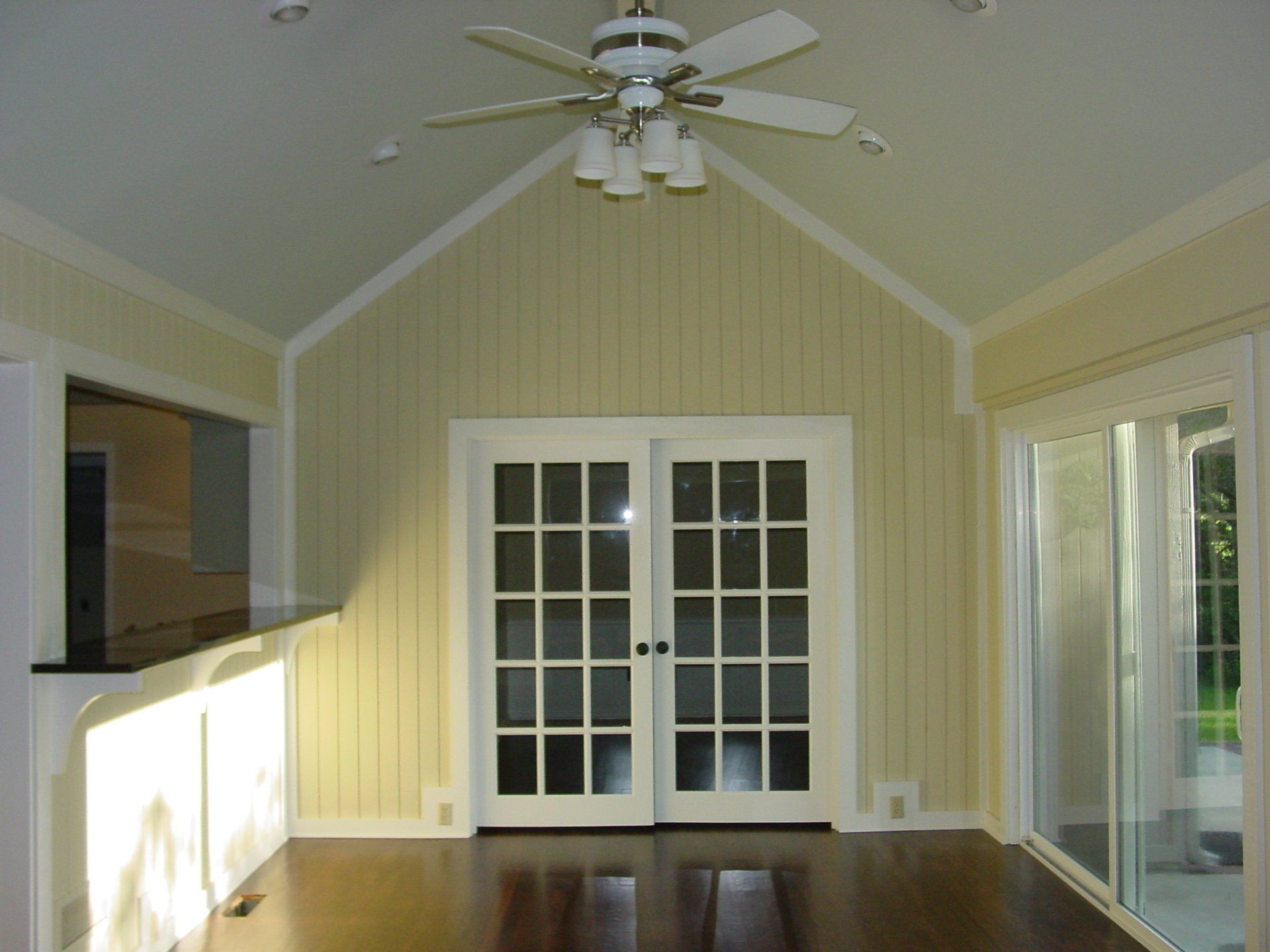 Interior of a light yellow room with dark wood floors, French doors, and a ceiling fan.