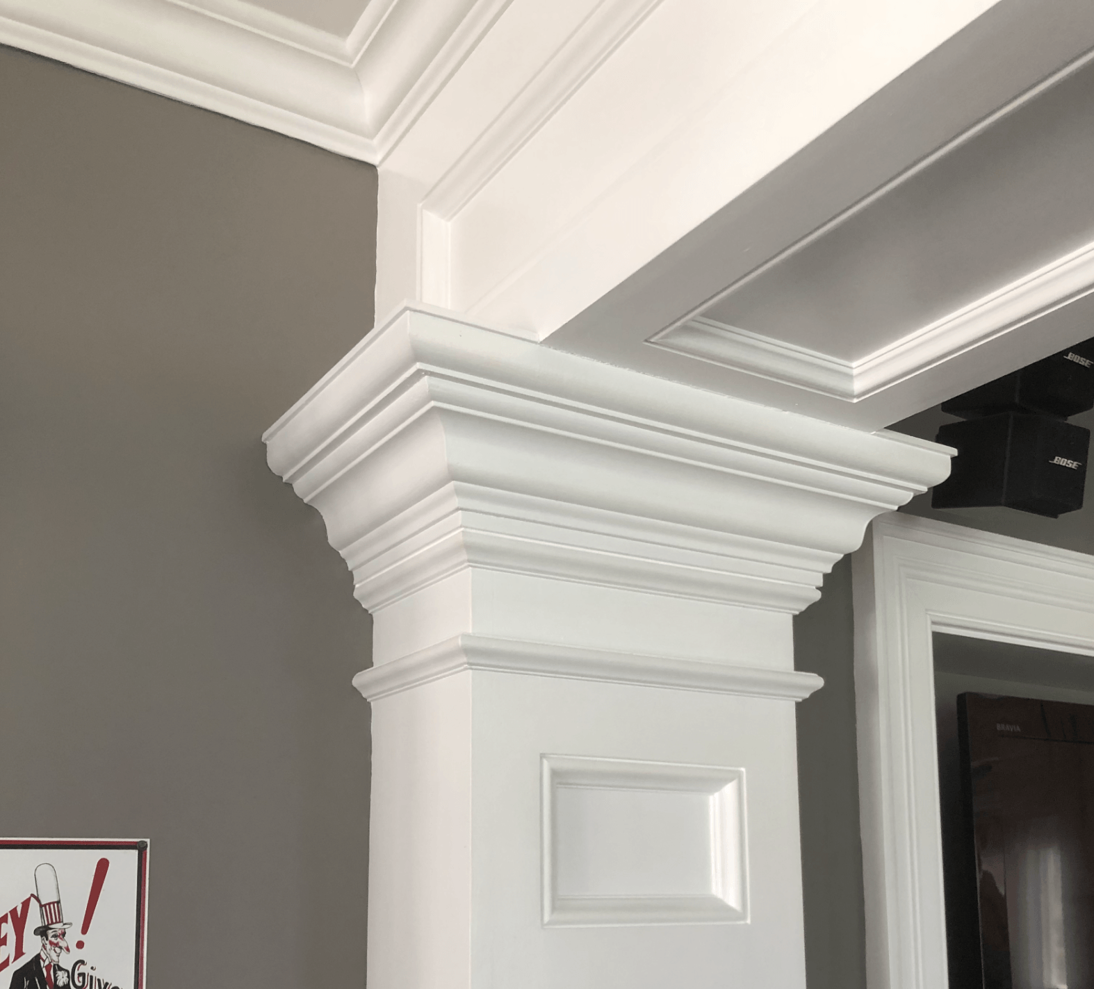 White, ornate molding surrounds a column against a gray wall. The molding forms a capital.