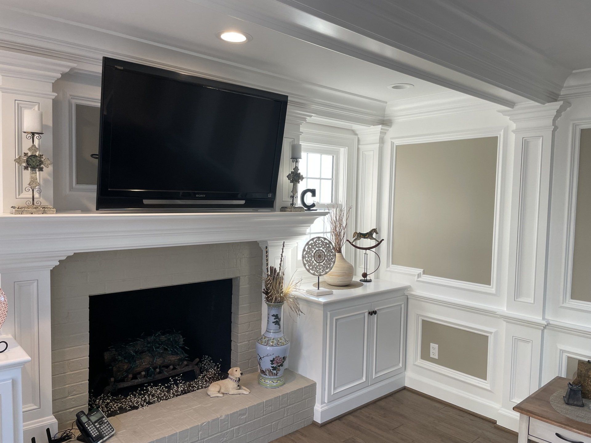 Fireplace with TV mounted above, white molding, decorative elements, and a cabinet.