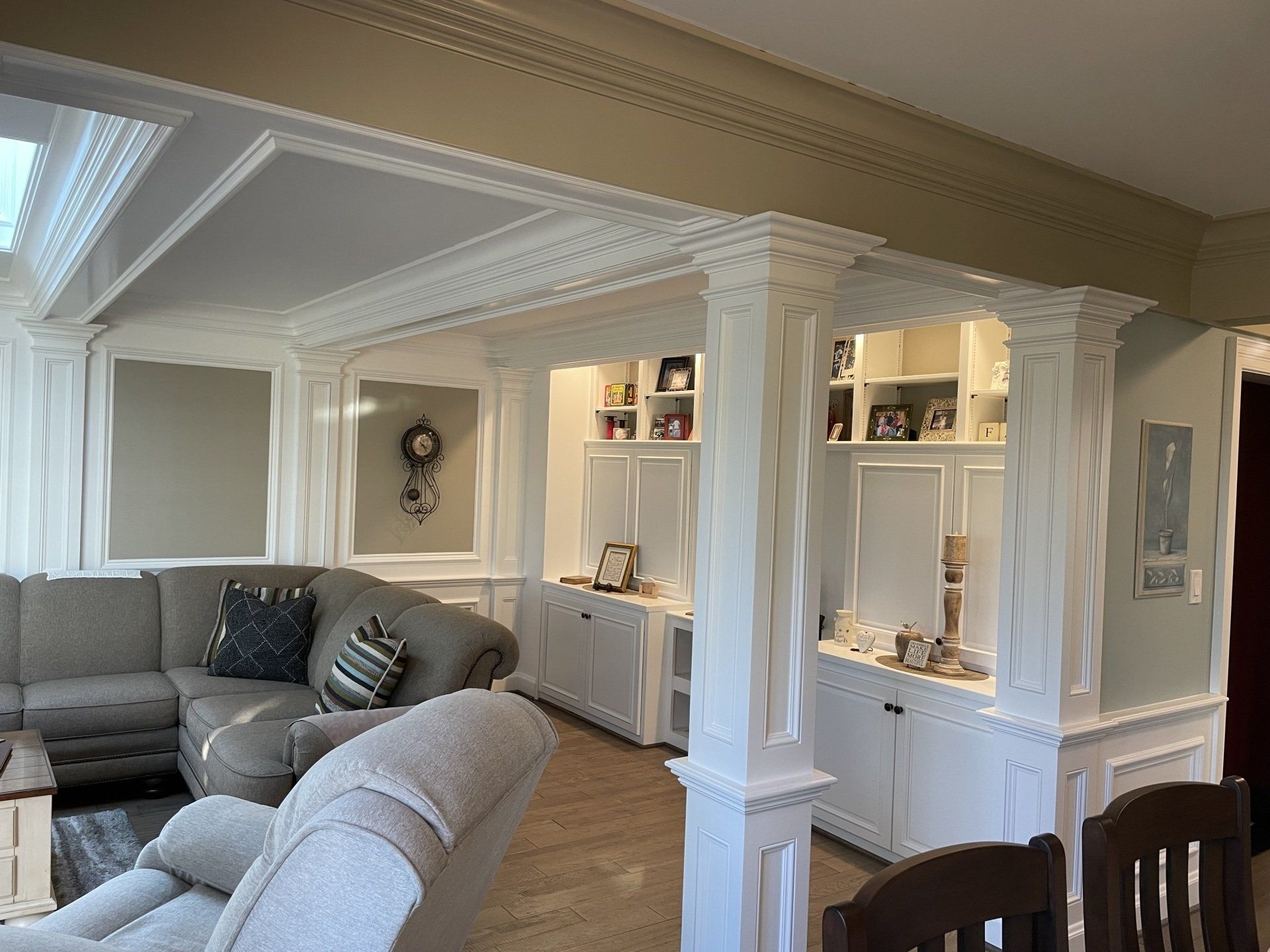 Living room with white built-ins, columns, and decorative moldings. A gray sectional sofa sits on the left.