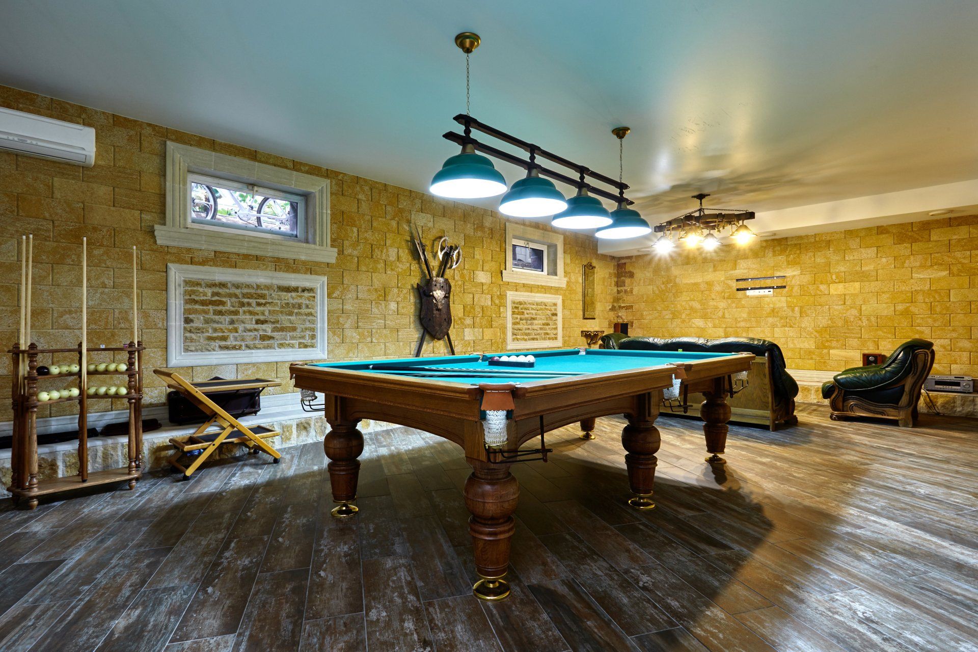 Pool table in a game room with stone walls, wood flooring, and pendant lighting.
