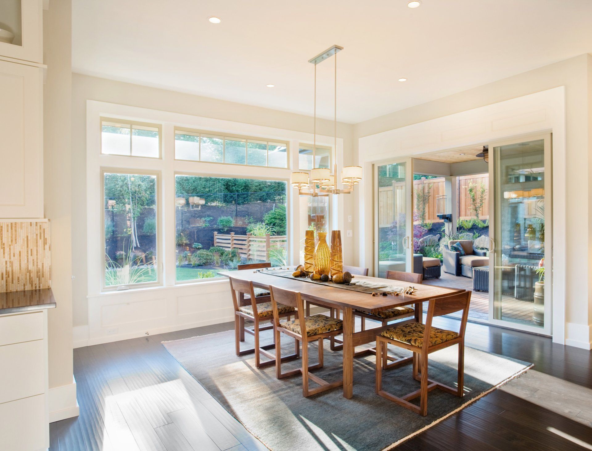 Dining room with wooden table, chairs, large windows overlooking a backyard patio.
