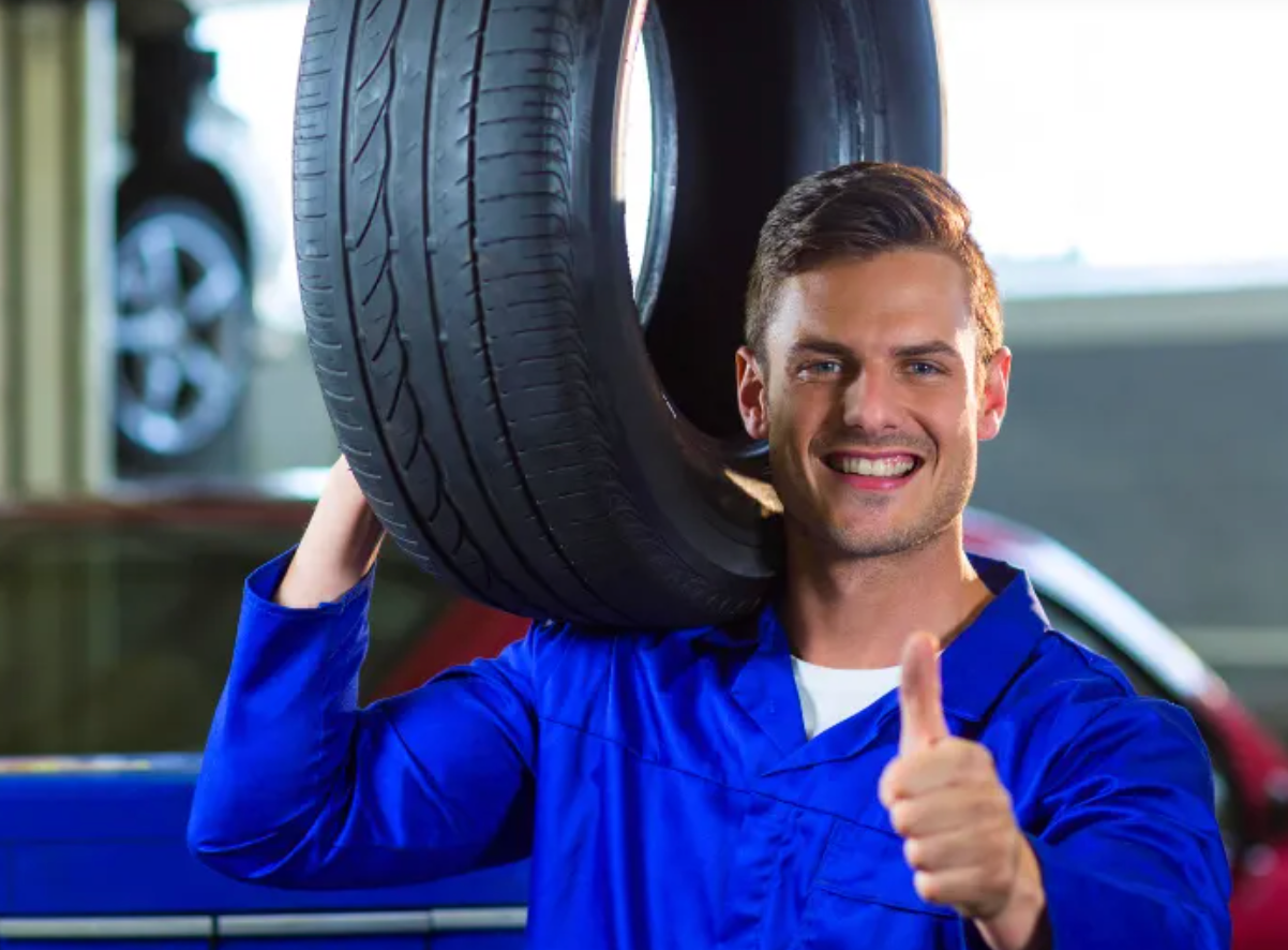 Um homem está segurando um pneu encima de seu ombro em uma garagem.