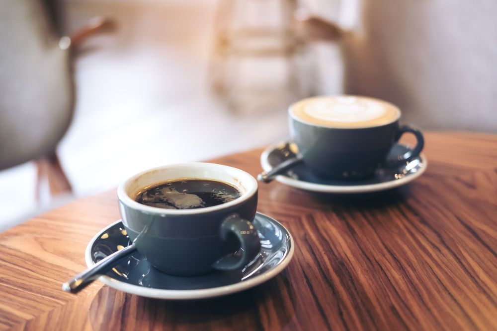 Two Cups of Coffee on Saucers Atop a Wooden Table — Kape Centro In Childers, QLD
