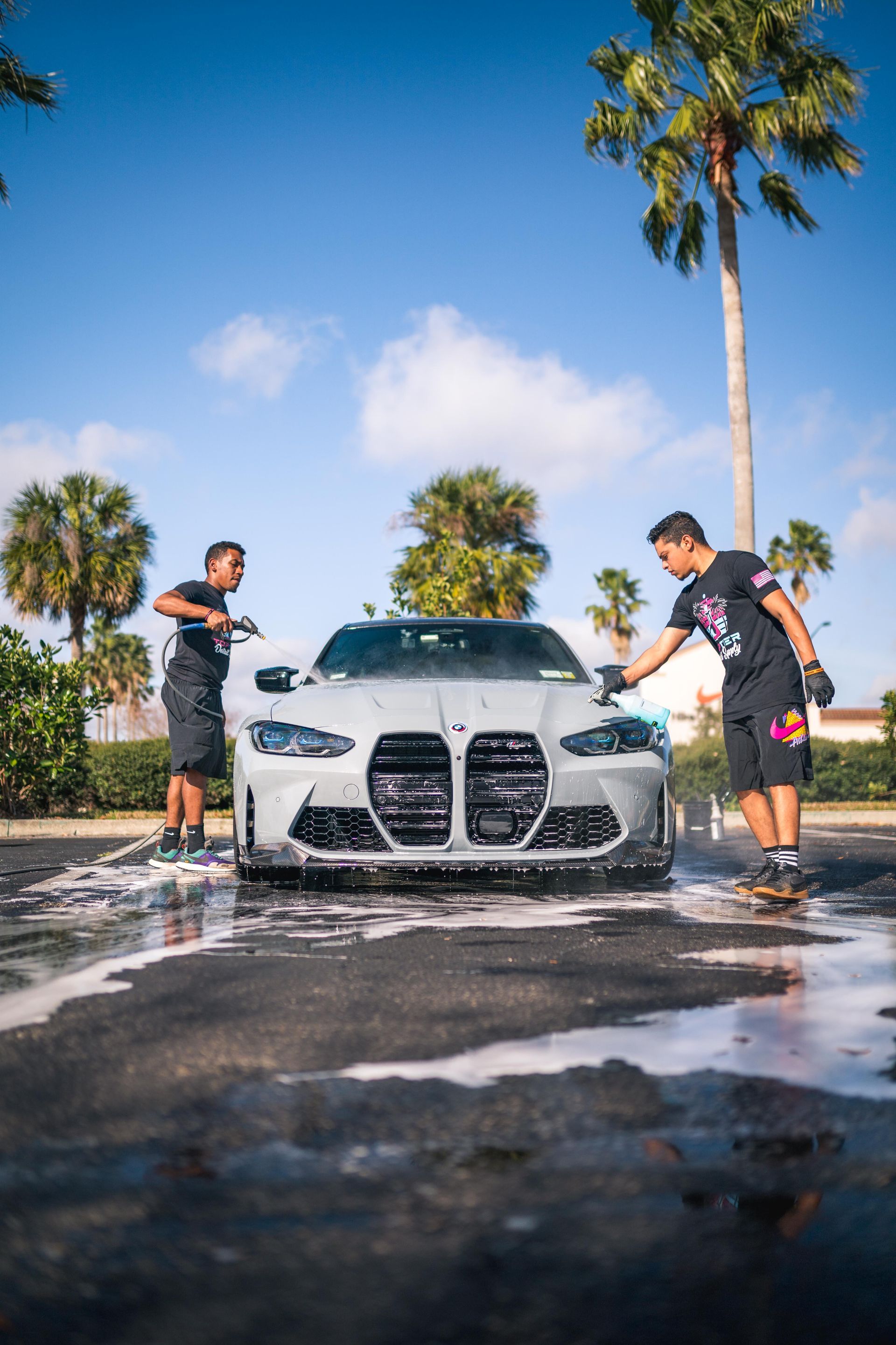 Two men are washing a bmw m4 in a parking lot.