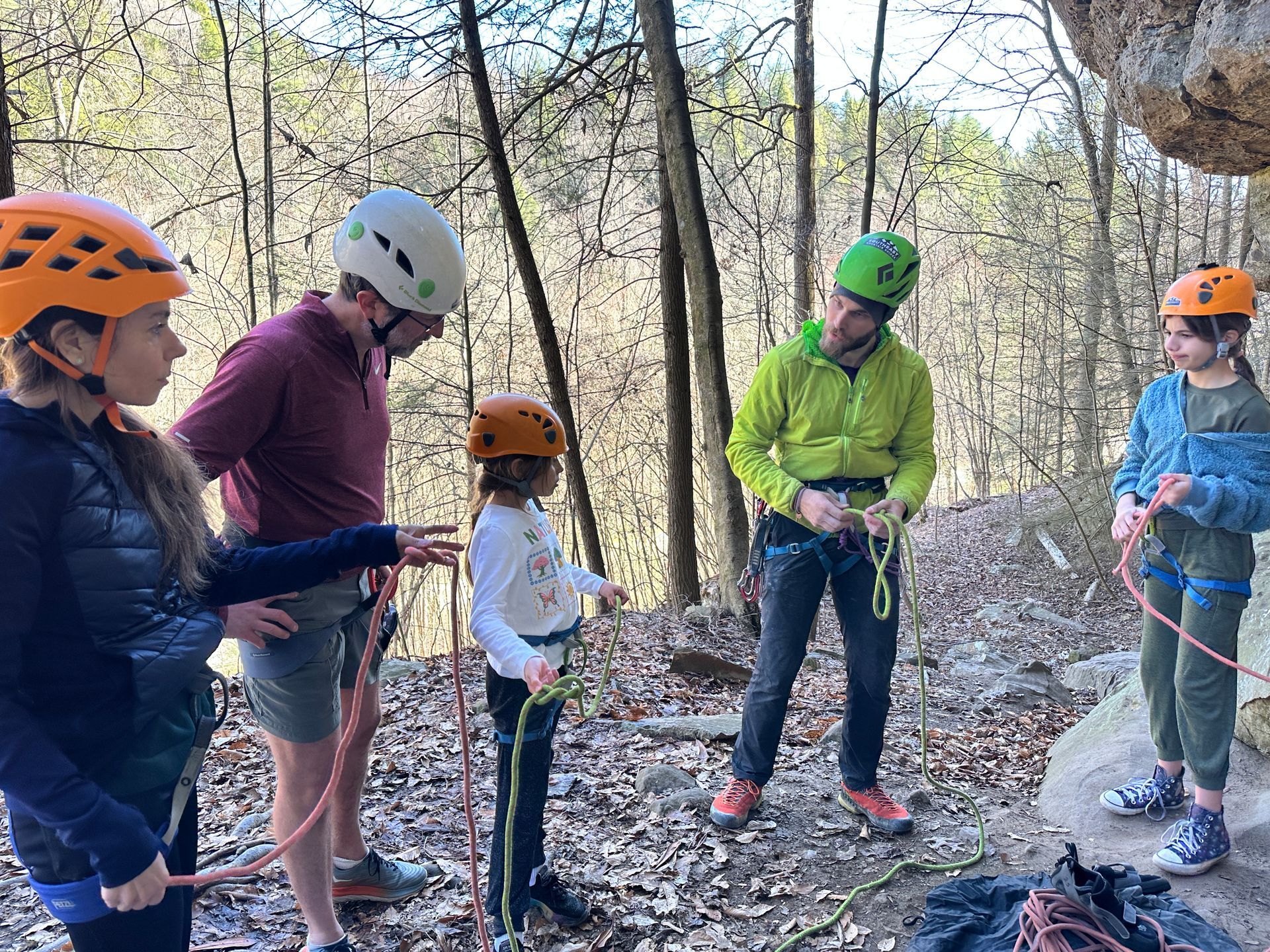 Climbing guide helping a client with harness and gear setup at the base of a crag in Red River Gorge