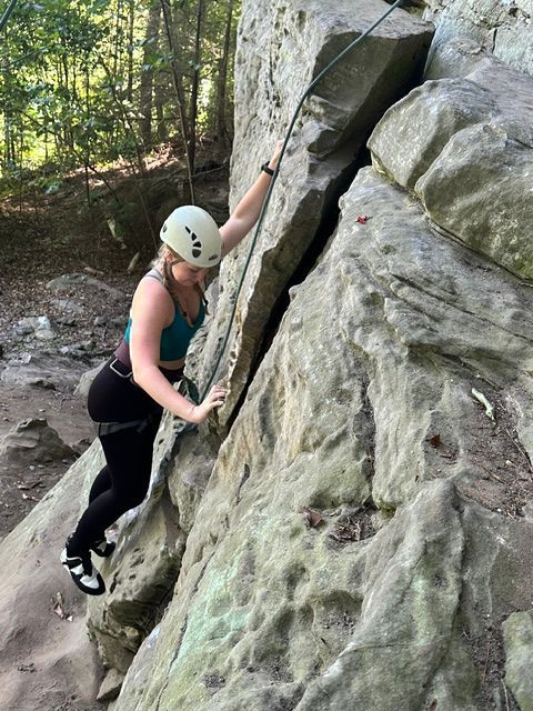 Female climber ascendsa route in the red river gorge clipped into a safety rope and smiling as she climbs the sandstone cliff.
