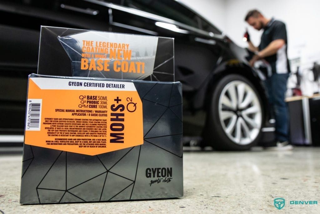 A man is polishing a car in a garage with a box of gyeon base coat in the foreground.