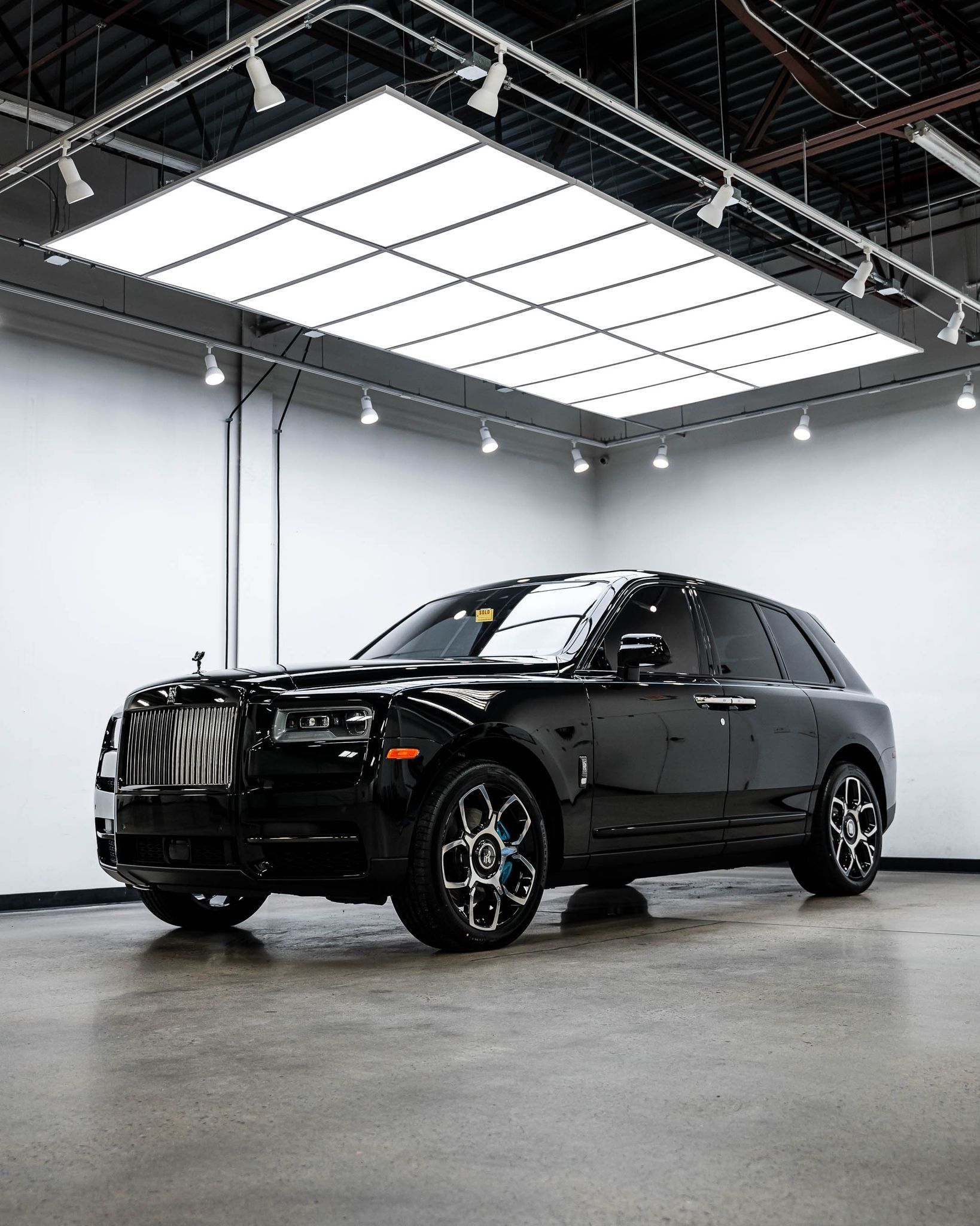 A black car is parked in a garage under a ceiling light.