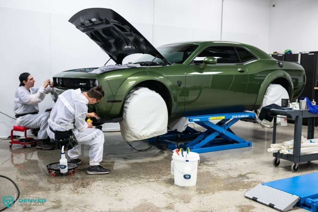 A group of men are working on a green dodge challenger in a garage.