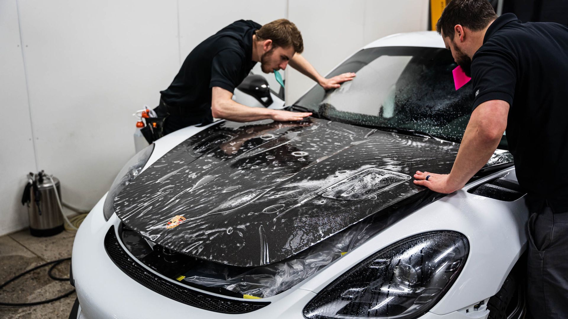 Two men are wrapping a white sports car with black plastic.