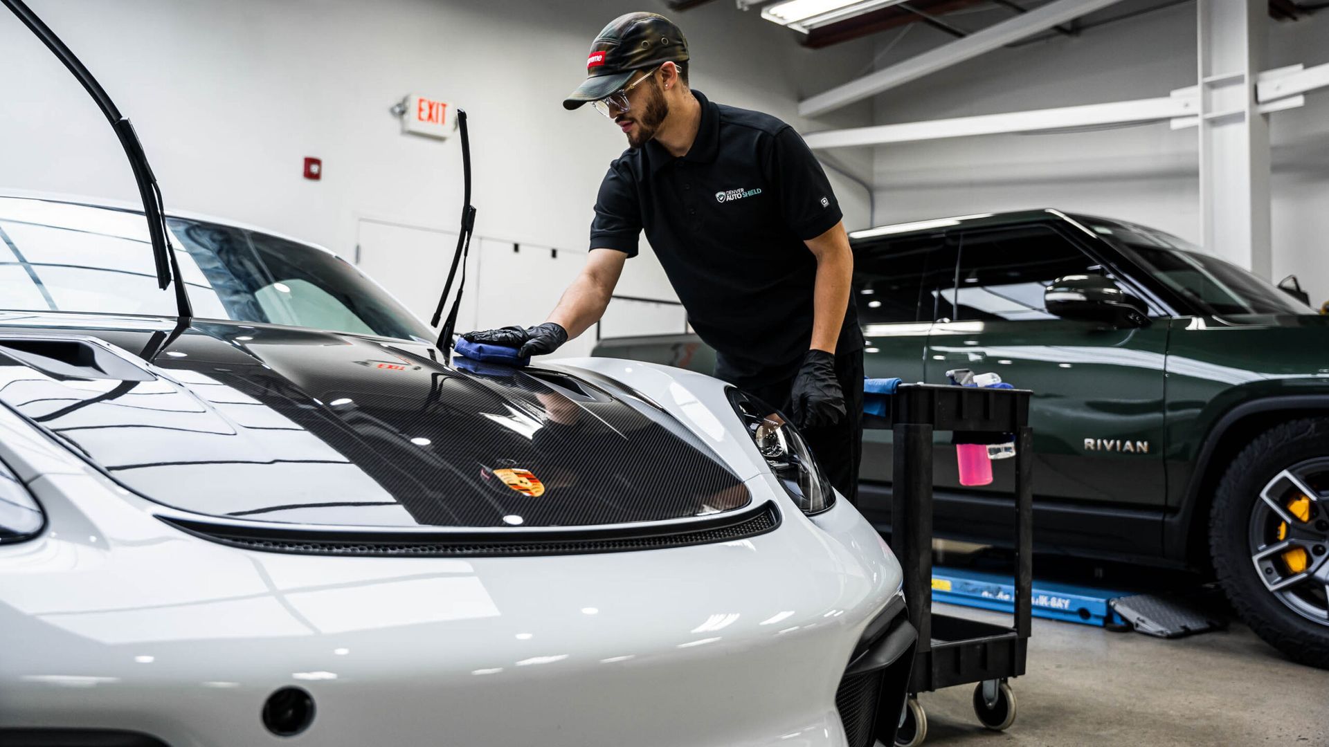 A man is cleaning the hood of a white car in a garage.