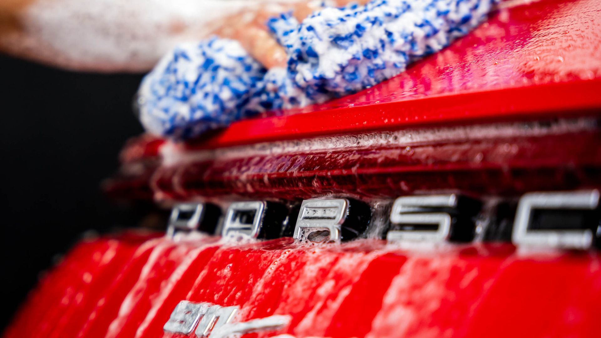 A person is washing a red porsche with a towel.