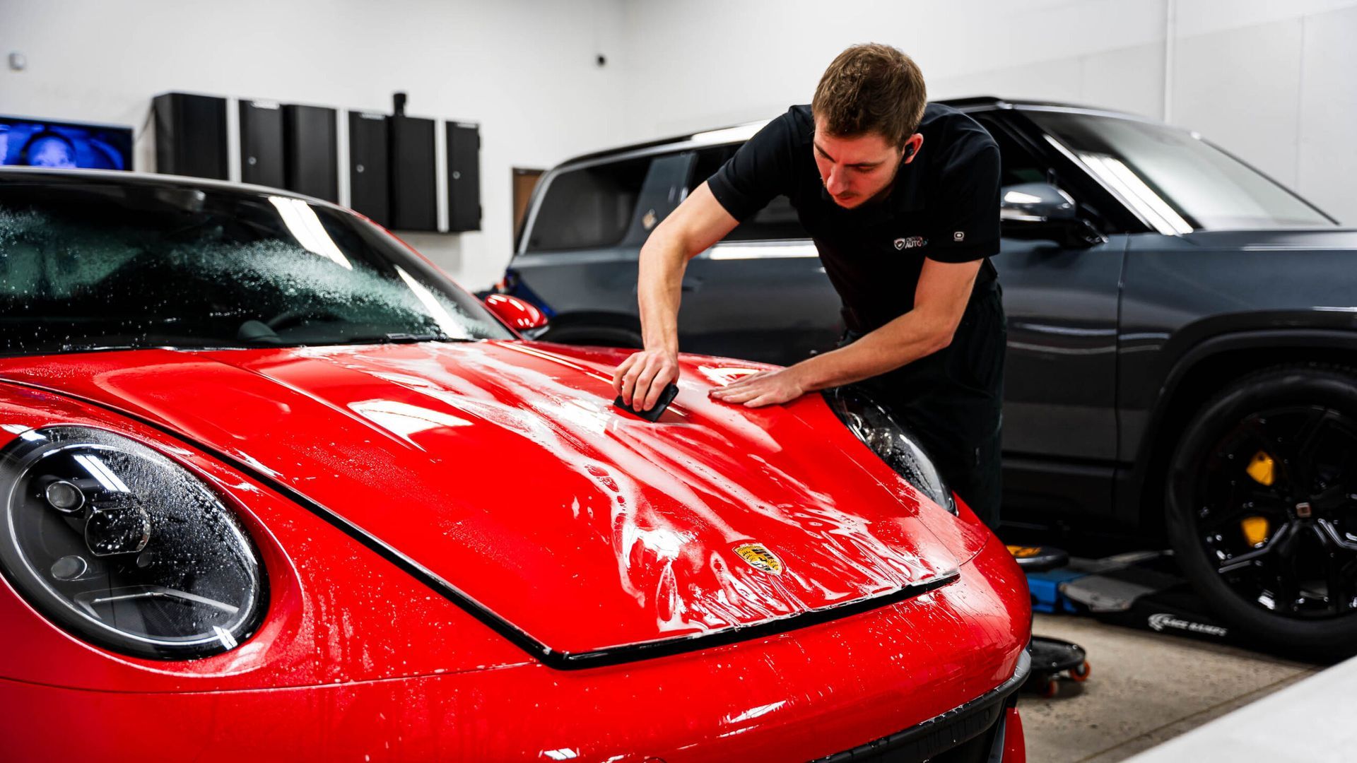 A man is polishing the hood of a red sports car in a garage.