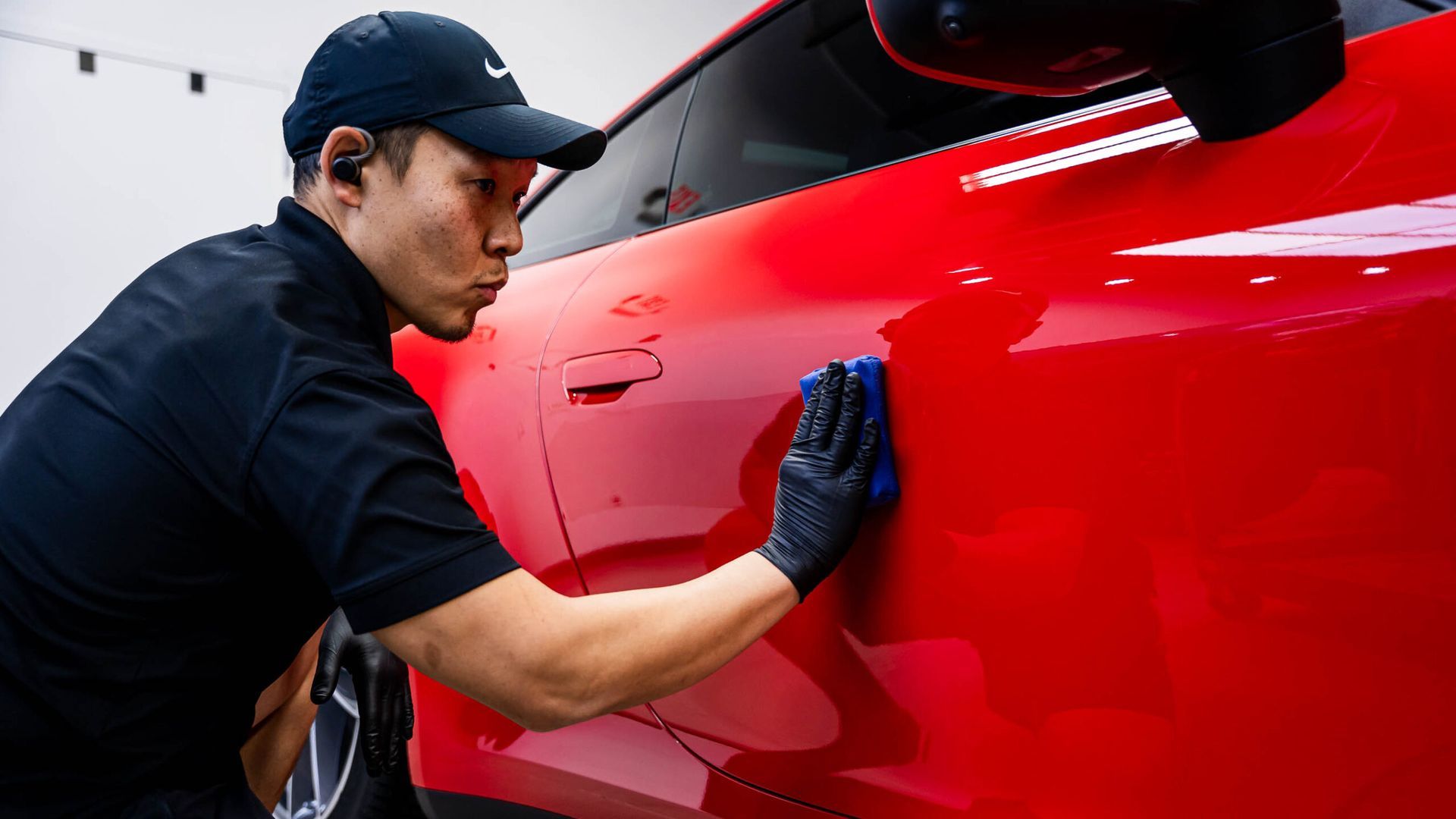 A man is cleaning a red car with a cloth.