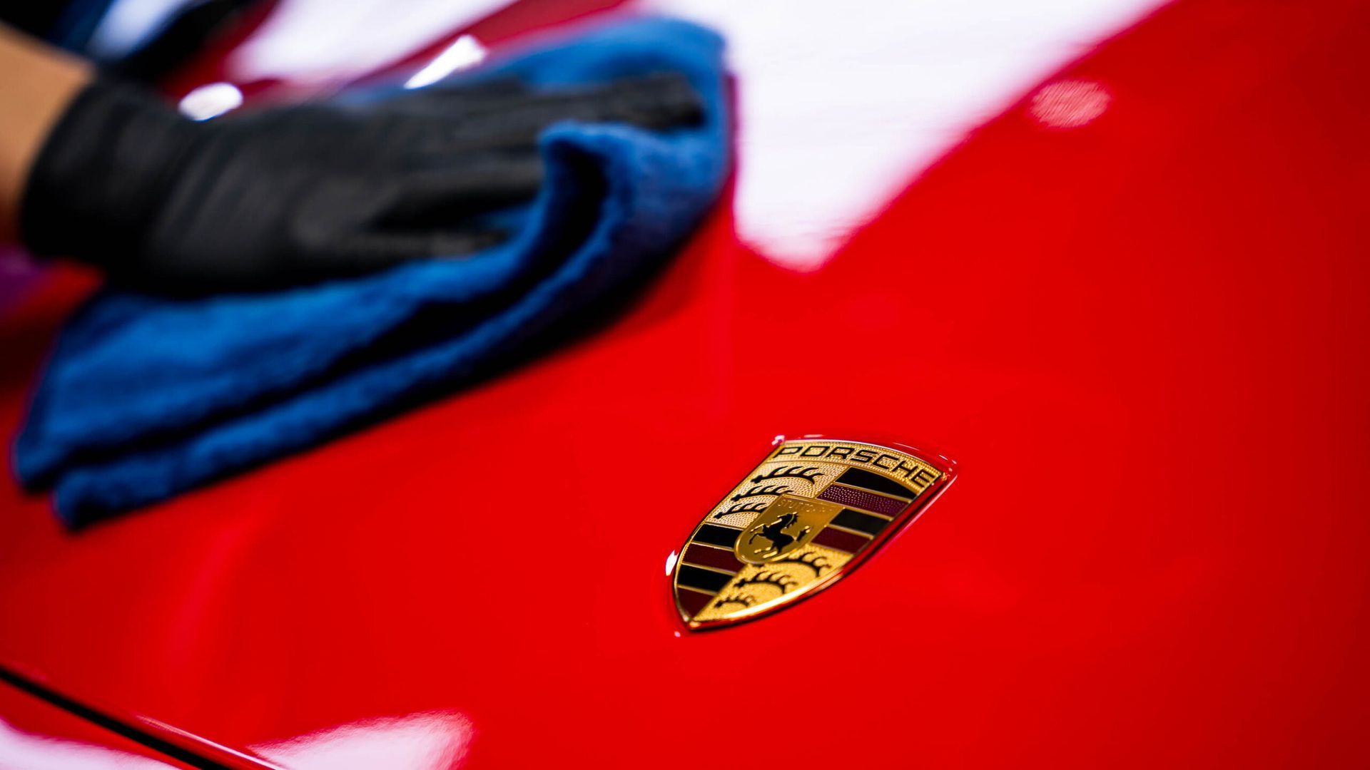 A person is cleaning a red porsche with a blue cloth.