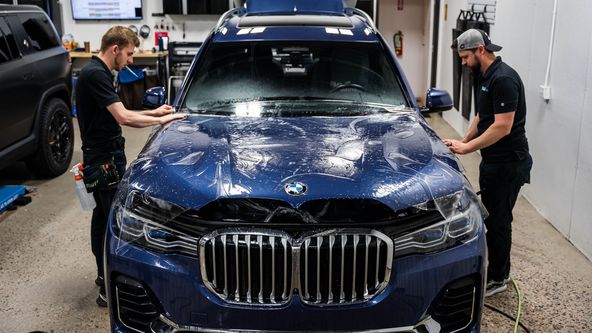 Two men are working on a blue car in a garage.