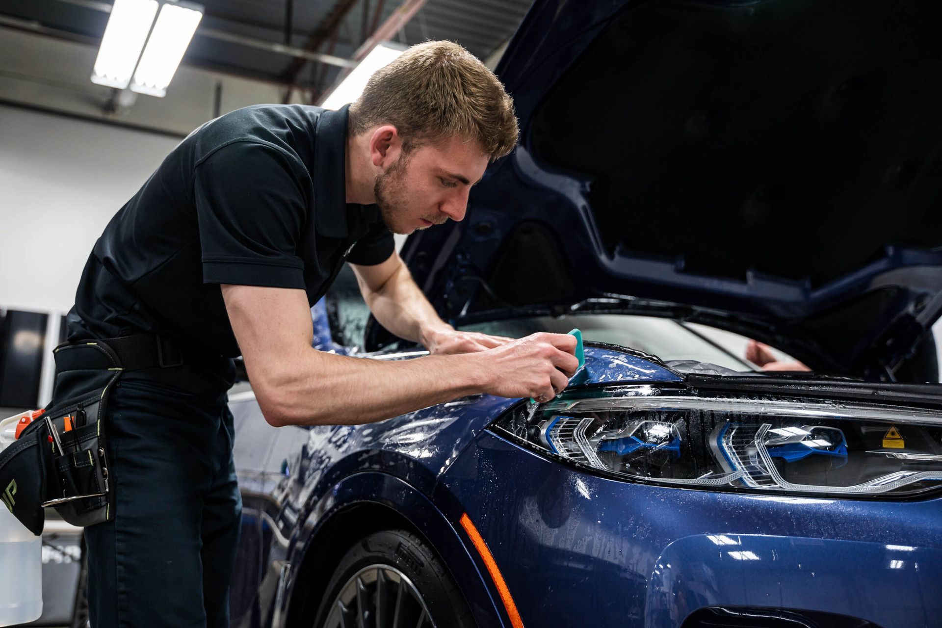 A man is working on a car with the hood open in a garage.