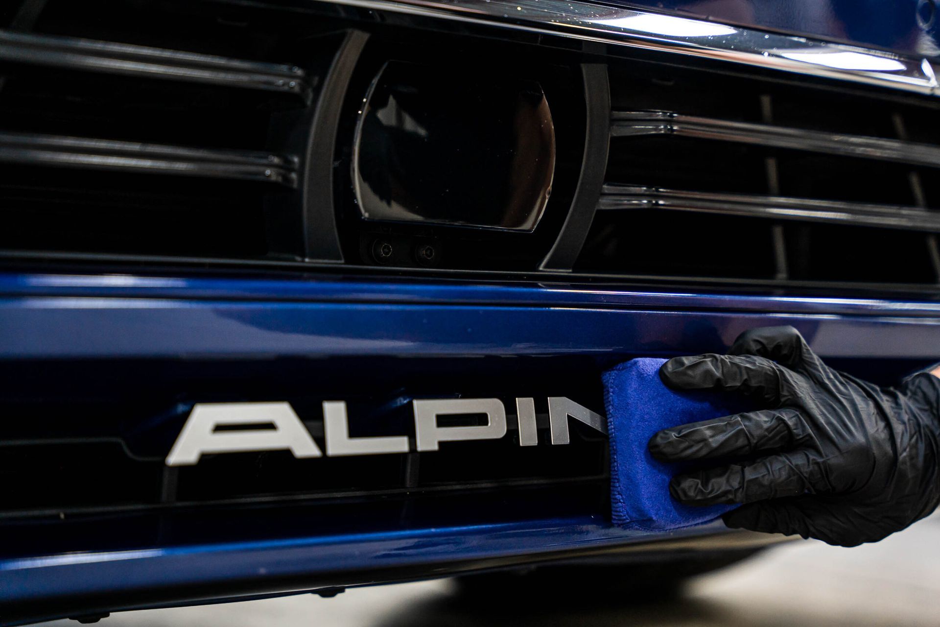 A person is cleaning the front of a blue alpina car.